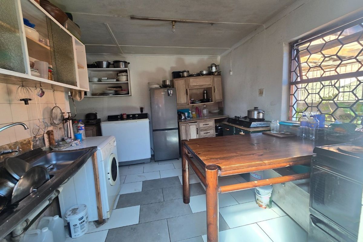 A functional kitchen space featuring tiled flooring, built-in cabinetry, and security burglar bars on the window, offering potential for modernization and renovation.
