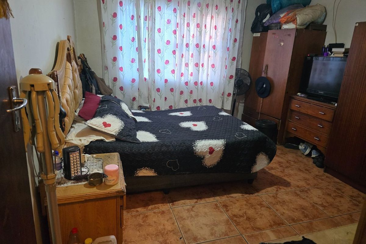 A bedroom featuring tiled flooring and window treatments, offering a functional space that could benefit from cosmetic updates and modern finishes.
