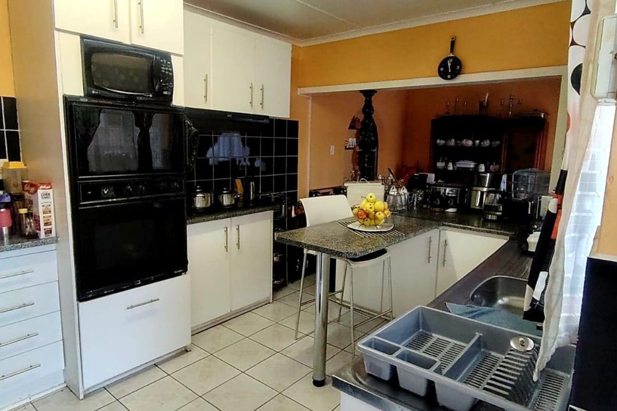 A functional kitchen featuring white cabinetry, granite countertops, built-in oven and microwave, and tiled flooring, with an open-plan layout connecting to the dining area.