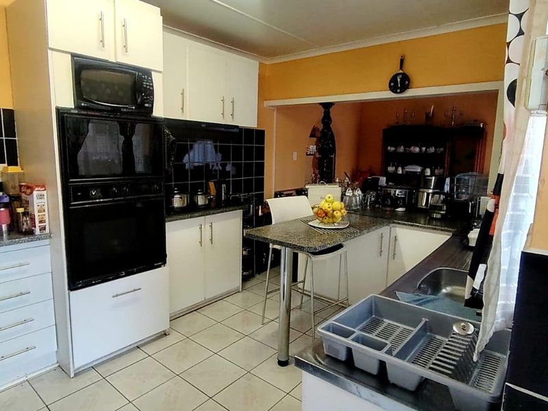 A functional kitchen featuring white cabinetry, granite countertops, built-in oven and microwave, and tiled flooring, with an open-plan layout connecting to the dining area.