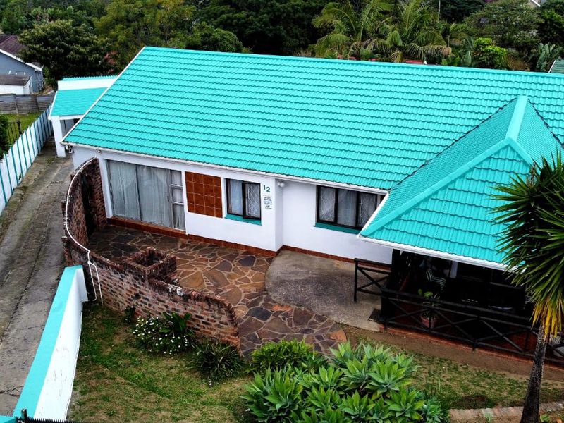 Aerial view of a residential property featuring a distinctive teal tiled roof, stone-paved patio area, and surrounding garden space.