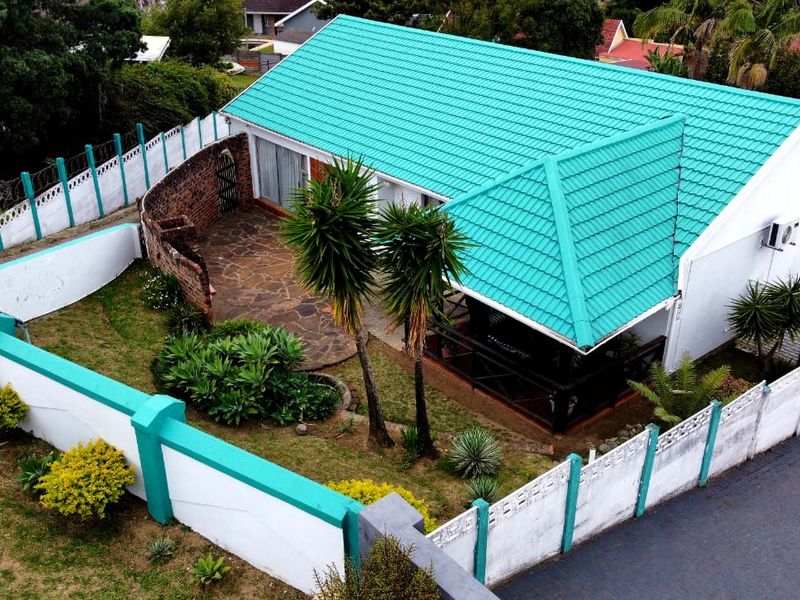 Aerial view of a residential property featuring a distinctive green tiled roof, a paved patio area, and a secure perimeter wall.