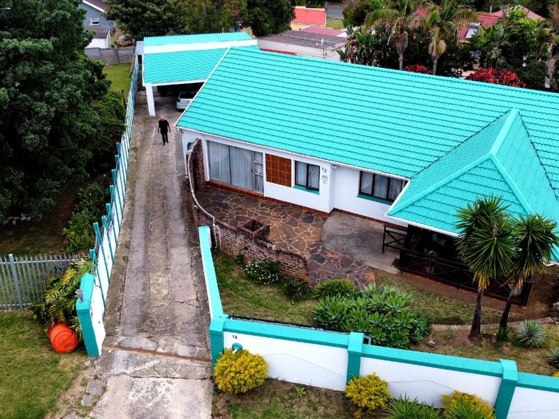 Aerial view of a residential property featuring a distinctive teal metal roof, concrete driveway, detached garage, and a stone-paved patio area.