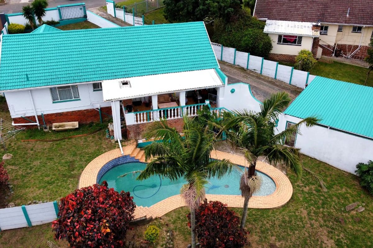 Aerial view of a residential property featuring a swimming pool, covered patio, and metal roofing, set within a fenced garden area.