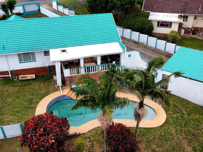 Aerial view of a residential property featuring a swimming pool, covered patio, and metal roofing, set within a fenced garden area.