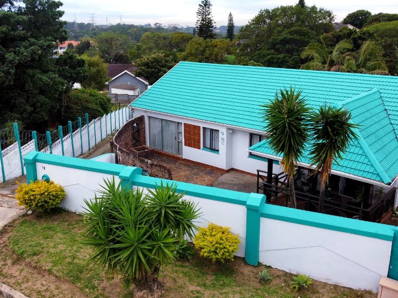 Aerial view of a residential property featuring a distinctive tiled roof, perimeter wall, and paved outdoor patio area set within a landscaped garden.