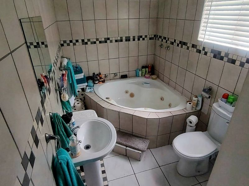A compact bathroom featuring a corner spa bath, pedestal basin, toilet, and tiled finishes throughout.