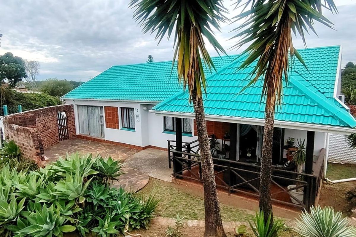 Rear view of the house featuring a covered patio, paved outdoor area, and distinctive teal tiled roof.