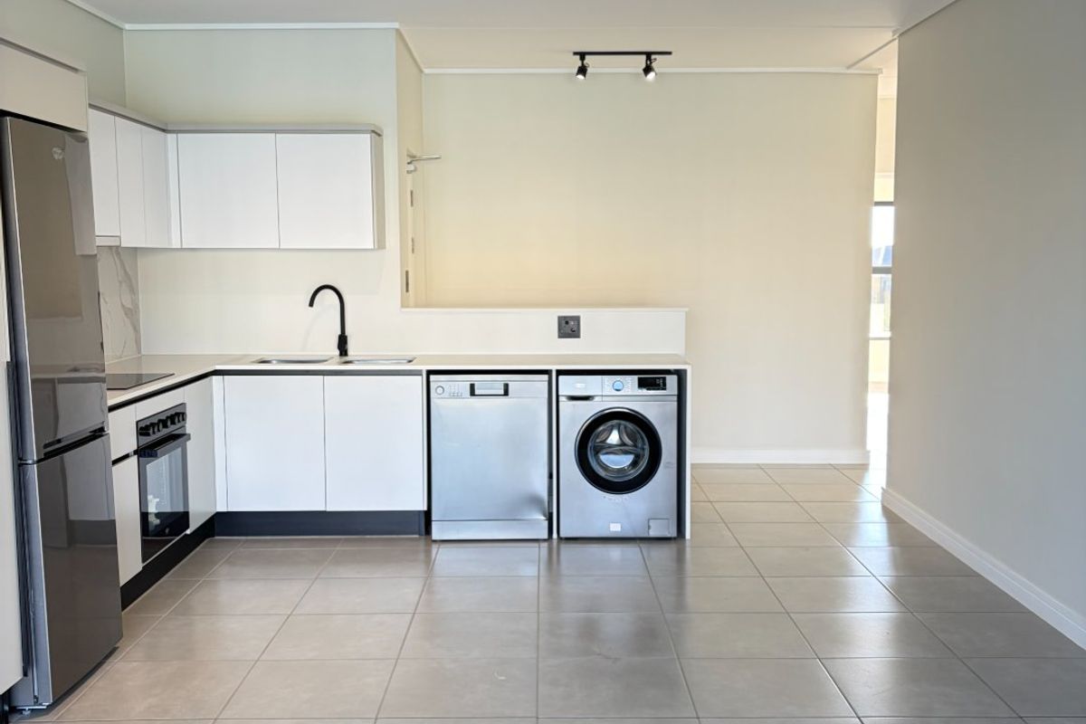 Modern open-plan kitchen featuring sleek white cabinetry, integrated appliances, tiled flooring, and contemporary track lighting in a clean, minimalist space.