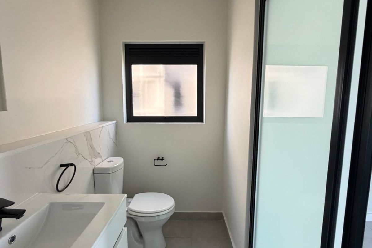 A modern, clean bathroom featuring a vanity with a marble-look splashback, a toilet, and a sleek frosted glass door.