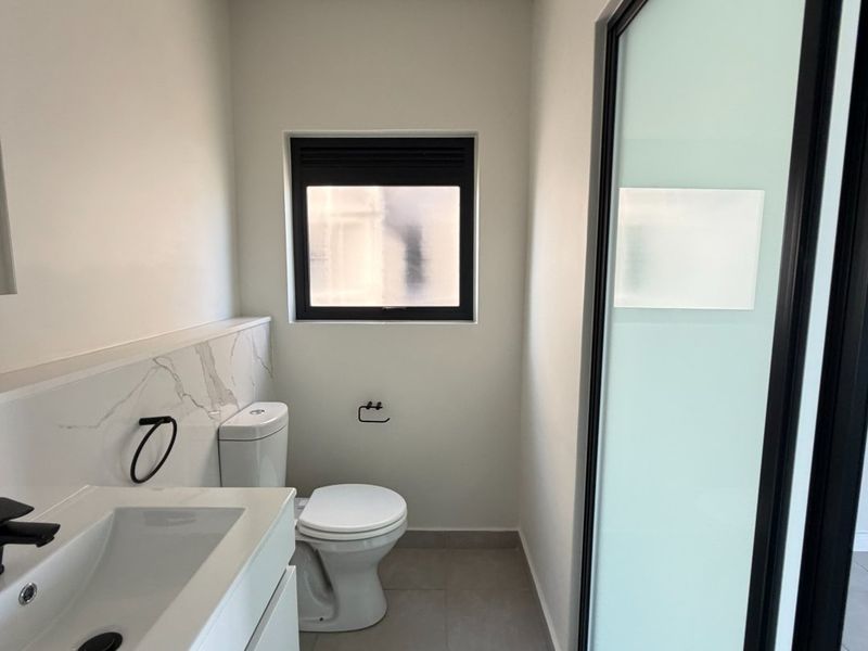 A modern, clean bathroom featuring a vanity with a marble-look splashback, a toilet, and a sleek frosted glass door.