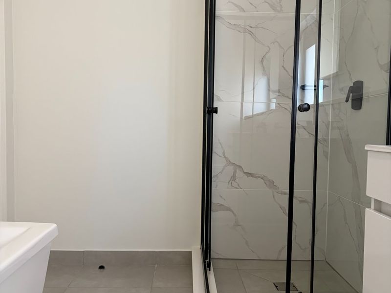 Modern bathroom featuring a walk-in shower with black-framed glass enclosure, marble-look wall tiling, and neutral grey floor tiles.