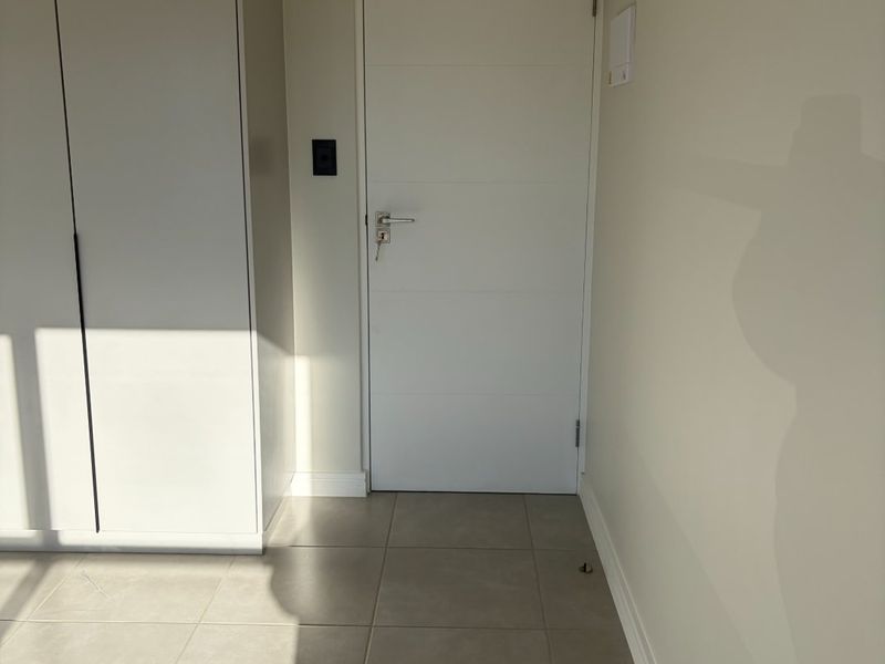 A clean, empty bedroom featuring neutral tiled flooring and a modern built-in wardrobe with a white finish.