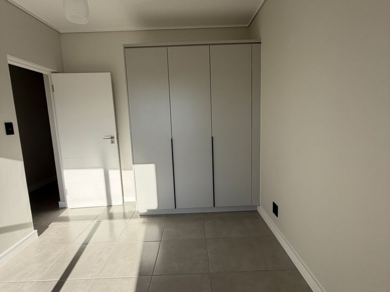 A bright, modern bedroom featuring neutral tiled flooring, a built-in wardrobe, and a minimalist pendant light fixture.