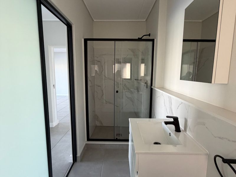 Modern bathroom featuring a walk-in shower with black frame, wall-mounted vanity with basin, and contemporary marble-look wall tiling.