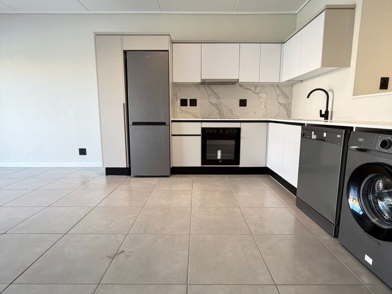 Modern, clean-lined kitchen featuring white cabinetry, marble-look splashback, built-in oven, extractor fan, and sleek tiled flooring in an open-plan layout.