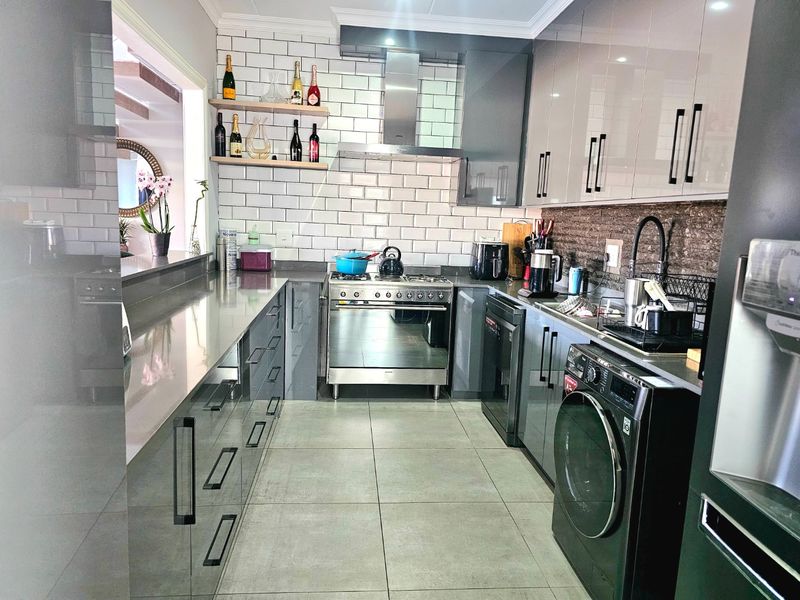 Modern kitchen featuring high-gloss cabinetry, subway tile backsplash, stainless steel gas stove, and stone countertops with integrated laundry appliances.
