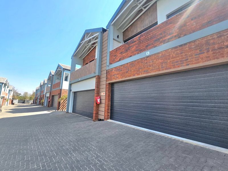 A row of modern townhouse units featuring brick facades, dark sectional garage doors, and paved driveway access.