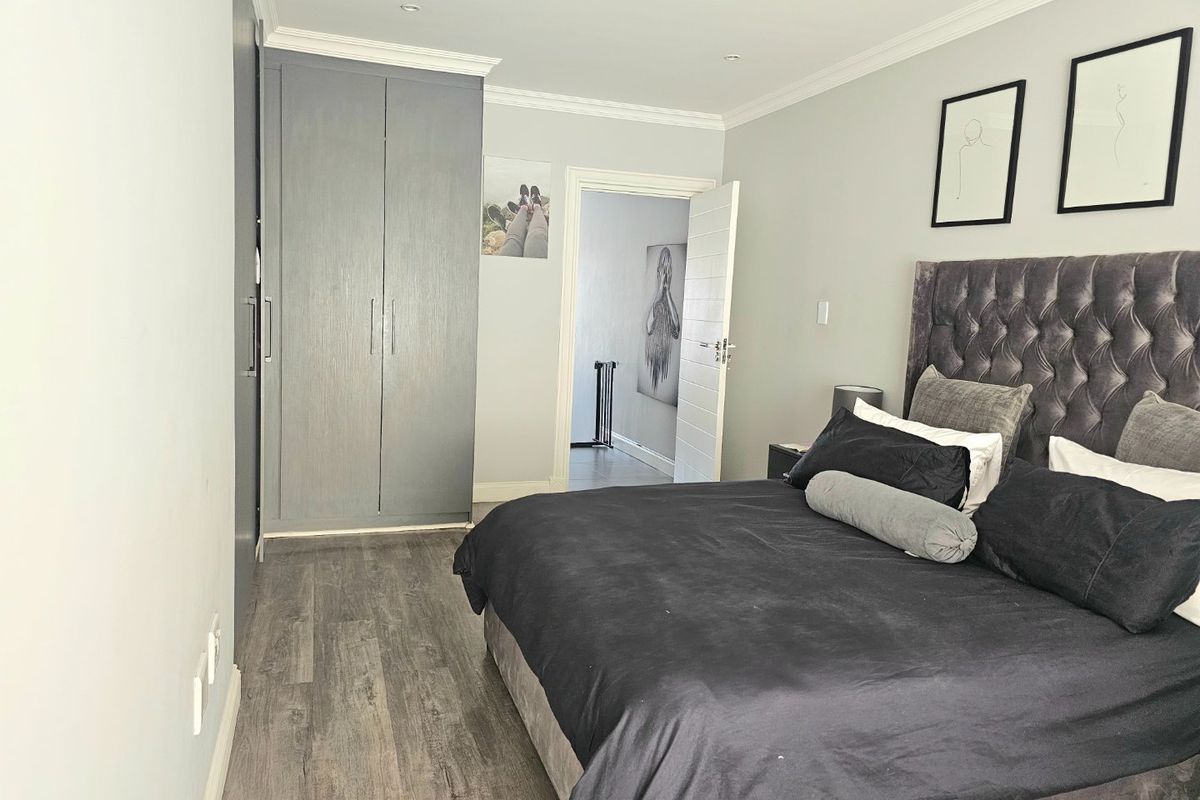 A well-maintained bedroom featuring modern grey built-in cupboards, laminate flooring, and elegant crown molding, offering a clean and contemporary living space.