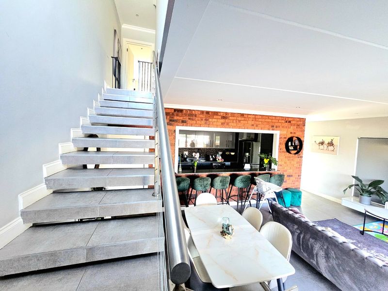 Spacious open-plan living area featuring a modern tiled staircase with stainless steel railing and an exposed brick wall overlooking the kitchen breakfast bar.