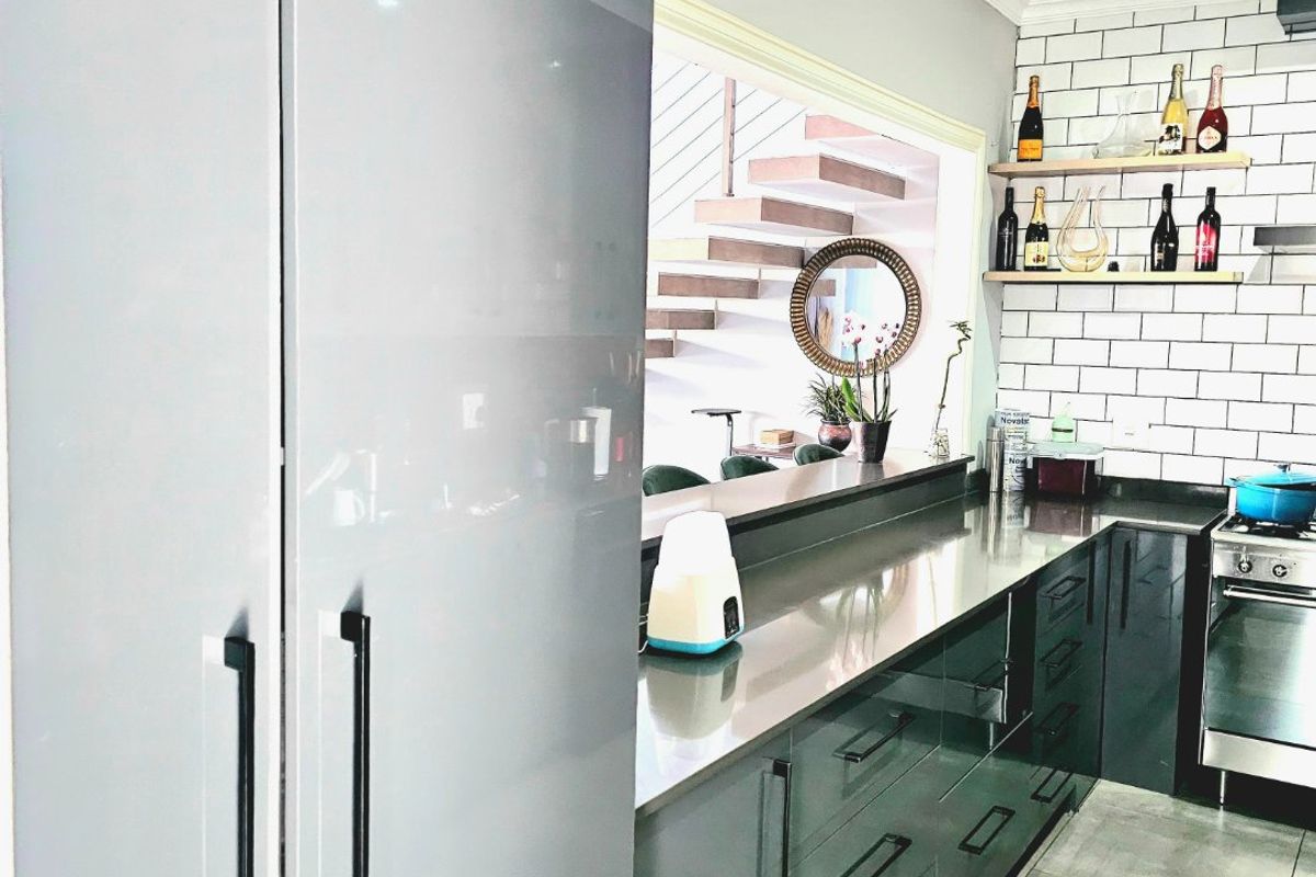 Modern kitchen featuring sleek grey cabinetry, stainless steel countertops, subway tile backsplash, and floating timber shelving, with an open view to the staircase.