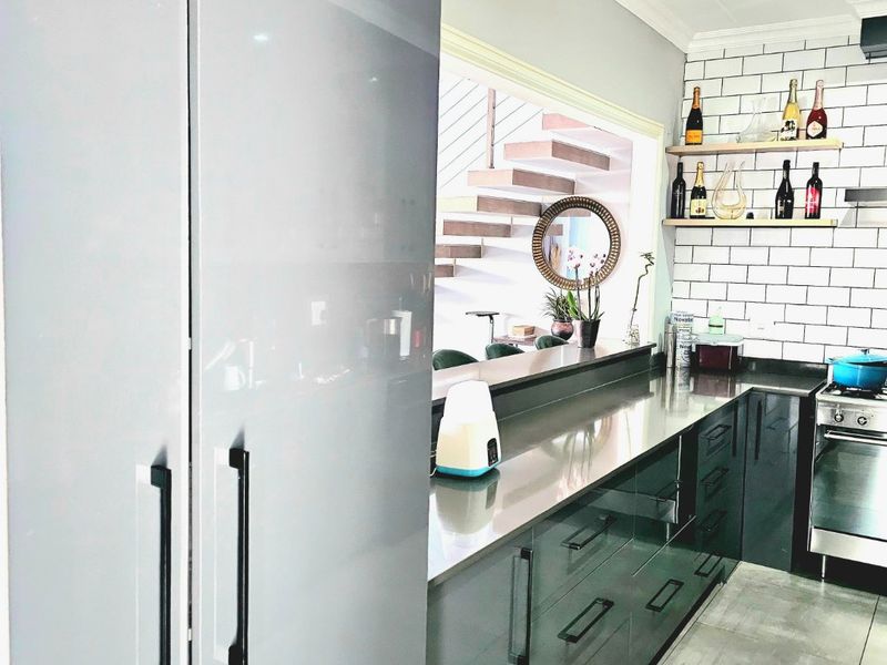 Modern kitchen featuring sleek grey cabinetry, stainless steel countertops, subway tile backsplash, and floating timber shelving, with an open view to the staircase.