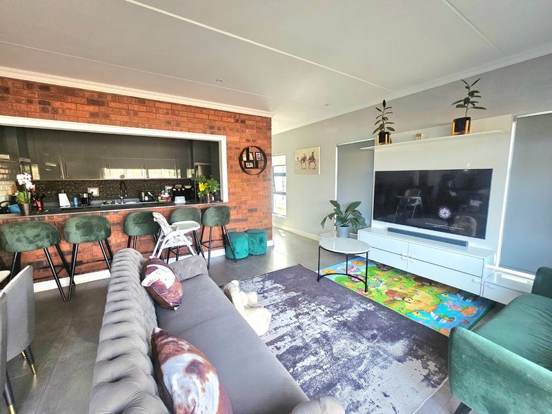 Open-plan living area featuring an exposed brick wall, integrated kitchen with breakfast bar, and modern tiled flooring, creating a functional and connected living space.