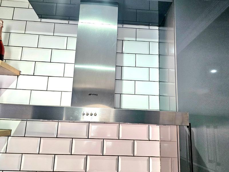 A modern kitchen featuring a stainless steel Smeg extractor fan and a clean white subway tile backsplash.