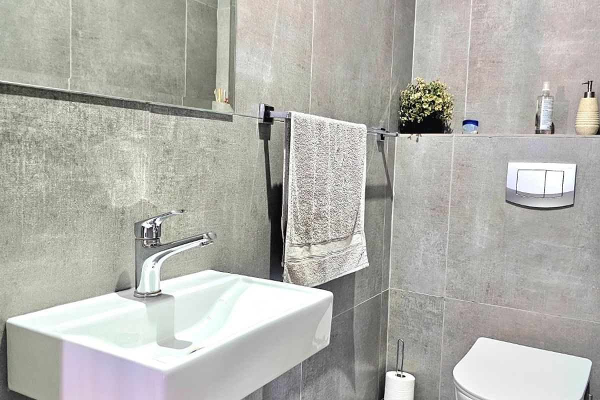 Modern bathroom featuring contemporary grey large-format tiling, a wall-mounted basin with chrome fixtures, and a sleek wall-hung toilet with a concealed cistern.