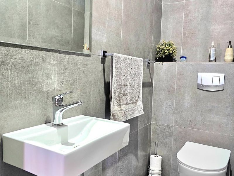 Modern bathroom featuring contemporary grey large-format tiling, a wall-mounted basin with chrome fixtures, and a sleek wall-hung toilet with a concealed cistern.