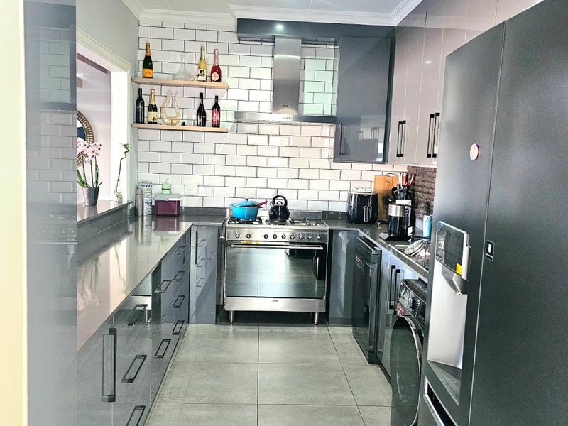 Modern galley-style kitchen featuring high-gloss cabinetry, stone countertops, a gas stove with extractor fan, and a classic subway tile backsplash.