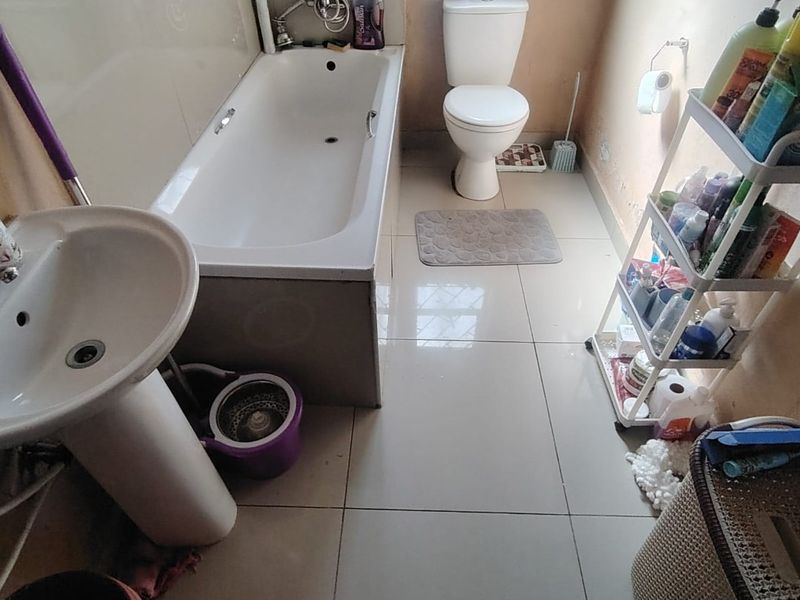 A functional bathroom featuring a pedestal basin, bathtub, and toilet with tiled finishes, currently showing signs of wear on the wall surfaces.