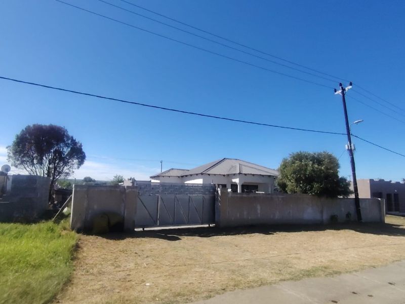 Front view of a residential property featuring a perimeter wall, metal gate, and tiled roof structure, set back from the street.
