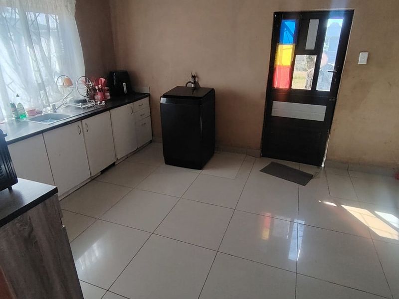 A functional kitchen area featuring tiled flooring, built-in cabinetry with a sink, and direct access to the exterior via a glass-paneled door.