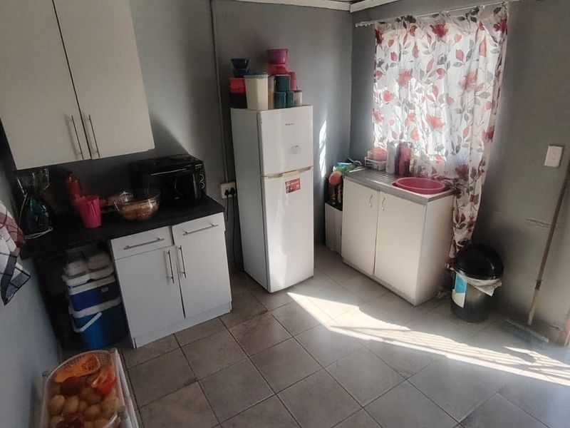 A compact kitchen featuring basic built-in cabinetry, laminate countertops, a stainless steel sink, and tiled flooring, requiring cosmetic updates to improve functionality and aesthetic appeal.
