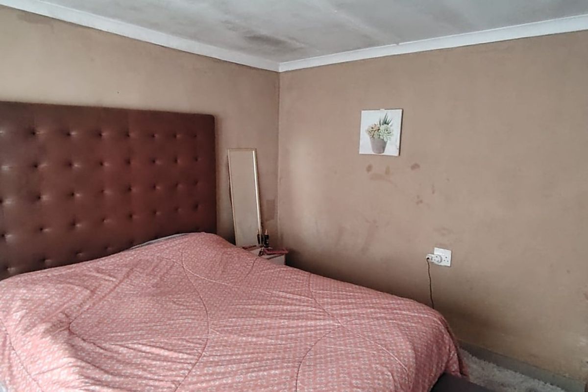 A bedroom featuring plain walls and a ceiling with visible signs of wear and staining, requiring cosmetic updates and maintenance.