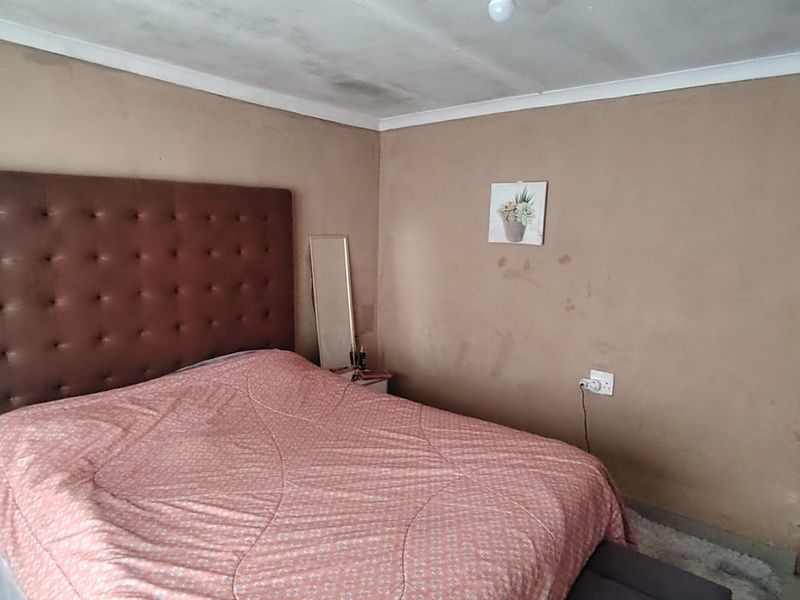 A bedroom featuring plain walls and a ceiling with visible signs of wear and staining, requiring cosmetic updates and maintenance.