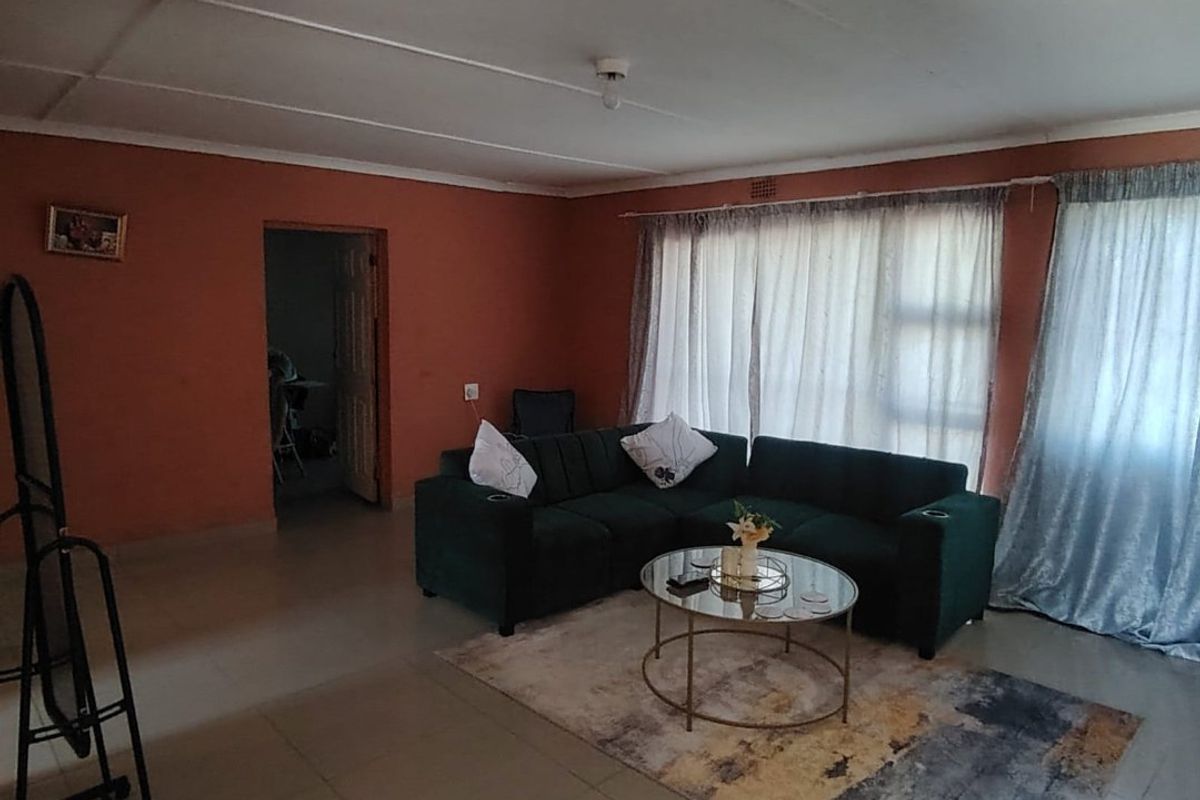 A living room featuring tiled flooring and ceiling panels, with large windows dressed in curtains, offering a functional space ready for cosmetic updates.
