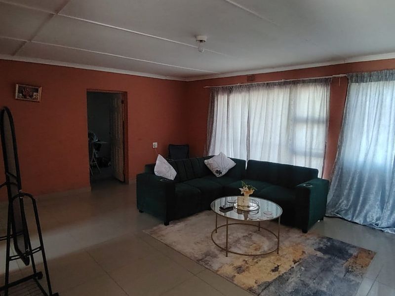 A living room featuring tiled flooring and ceiling panels, with large windows dressed in curtains, offering a functional space ready for cosmetic updates.