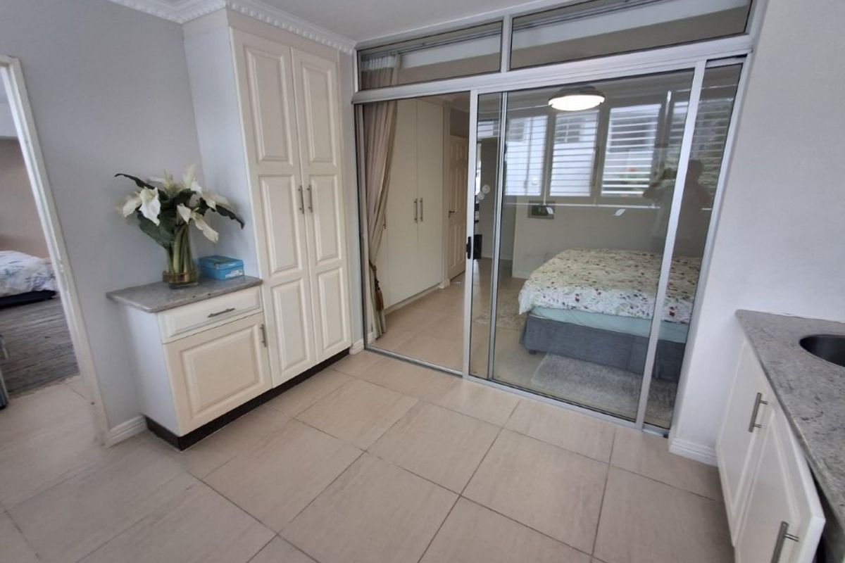 A bright living area featuring neutral tiled flooring, crown molding, and built-in cabinetry, with a sliding glass door providing access to the bedroom.