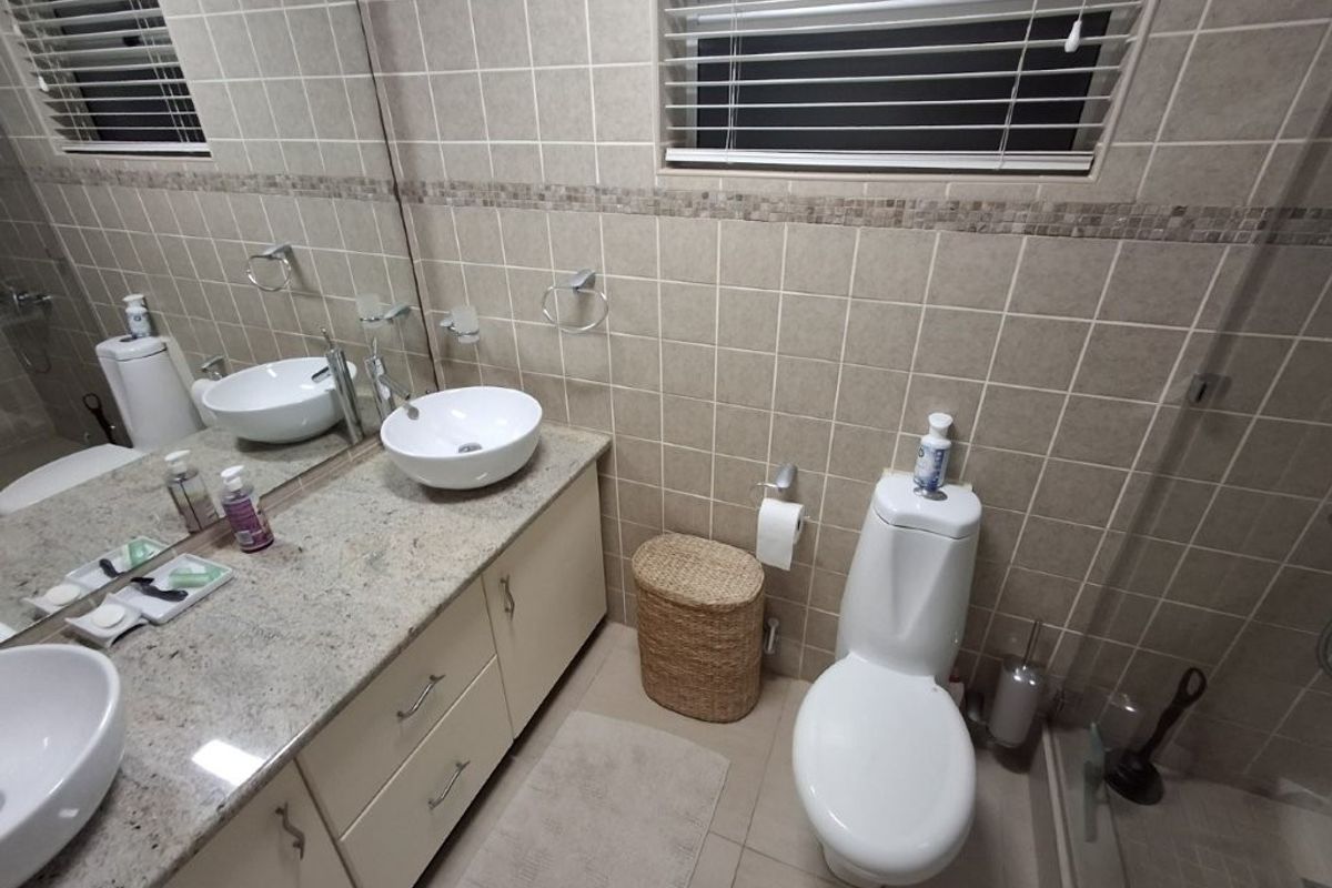 A well-maintained bathroom featuring a granite vanity with dual vessel sinks, neutral ceramic tiling, and modern fixtures.