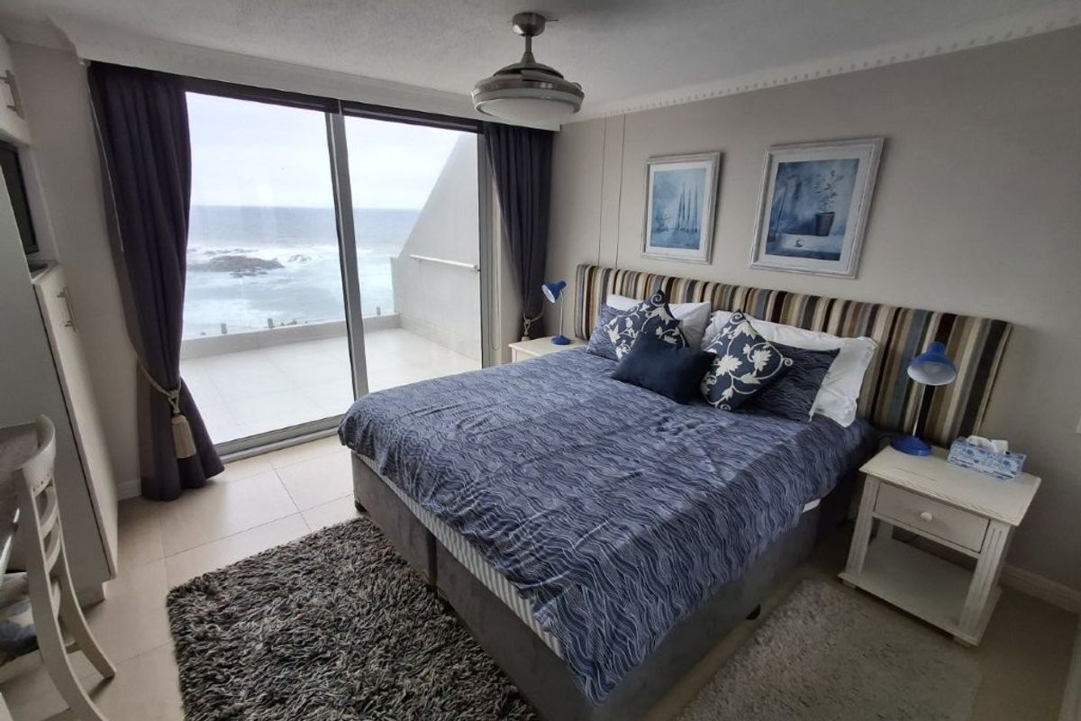 A well-maintained bedroom featuring tiled floors, a ceiling fan, and large sliding glass doors that open onto a balcony with ocean views.