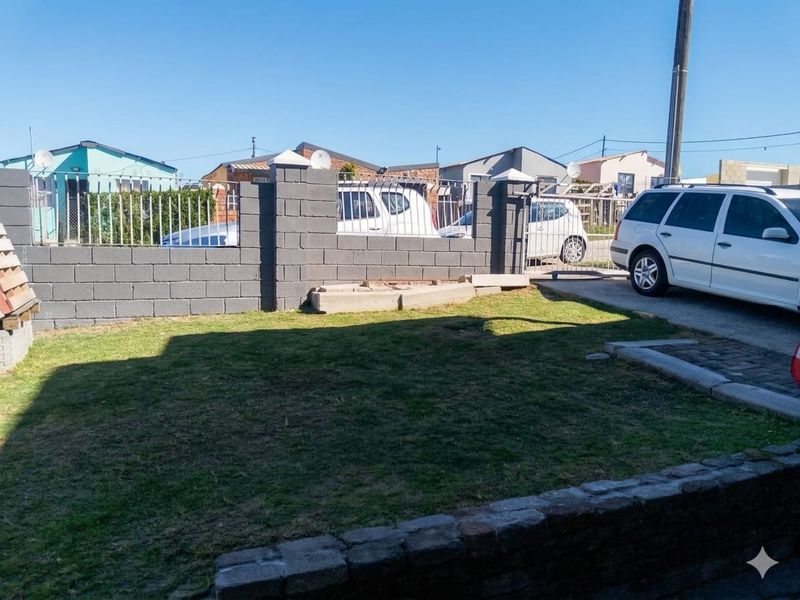Front yard area featuring a concrete block boundary wall with metal fencing, a paved driveway, and a grass lawn.