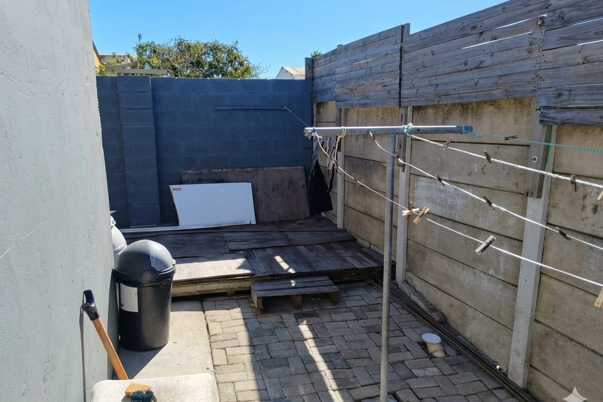 A functional rear courtyard area featuring paved flooring, a concrete block boundary wall with timber fencing, and a fixed rotary clothesline.