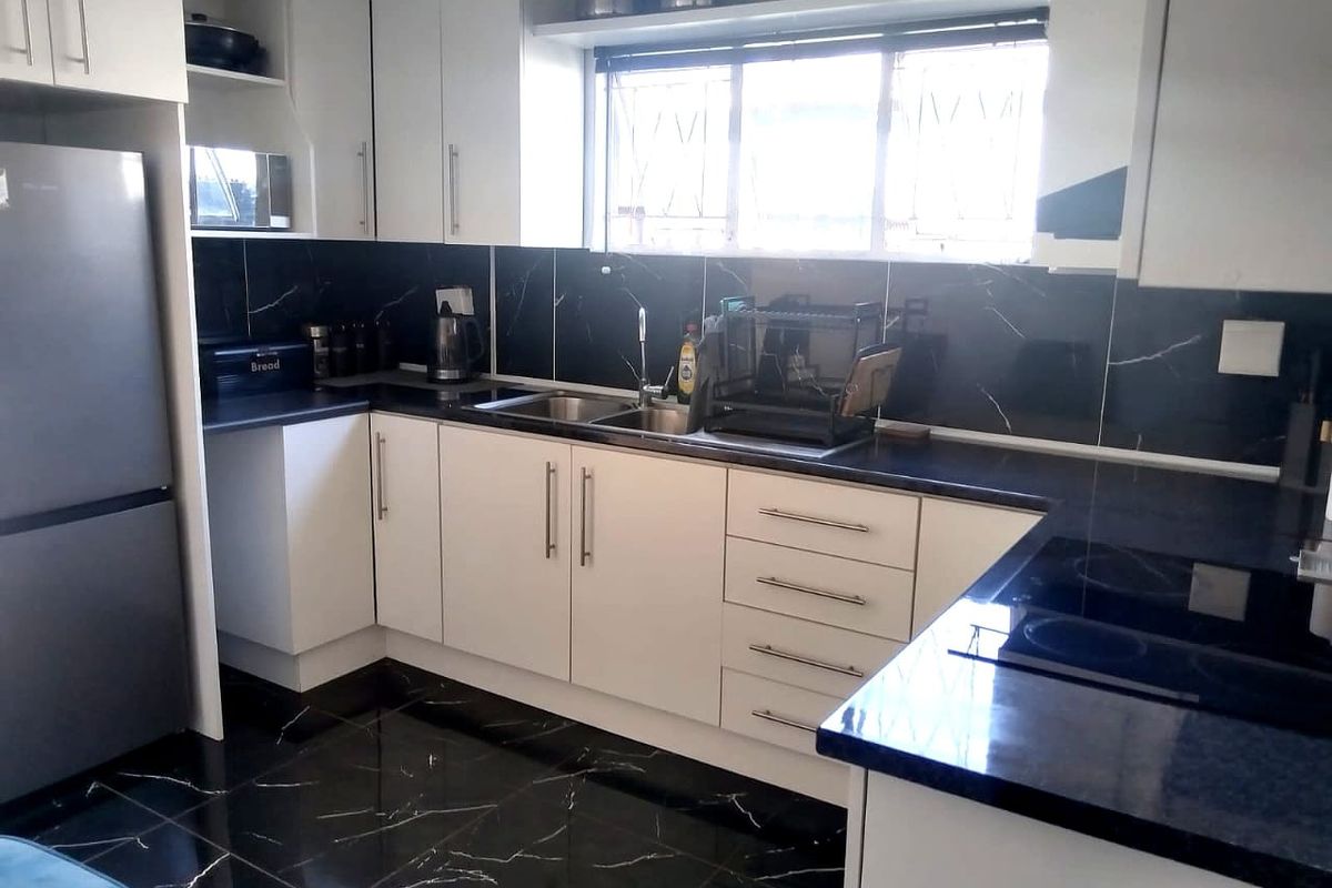 Modern kitchen featuring white cabinetry, contrasting black marble-effect splashbacks and flooring, double sink, and integrated hob with ample counter space.