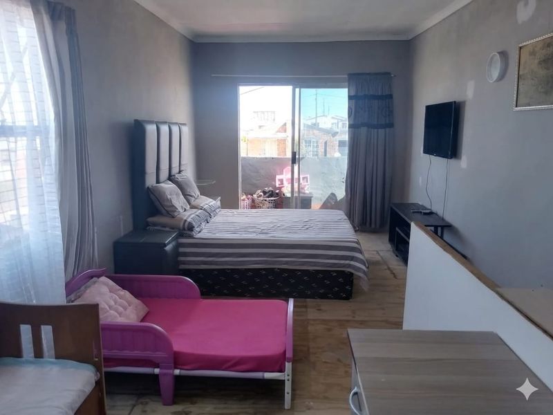 A bedroom featuring laminate flooring and a sliding glass door leading to an outdoor area, with walls requiring finishing and paint.