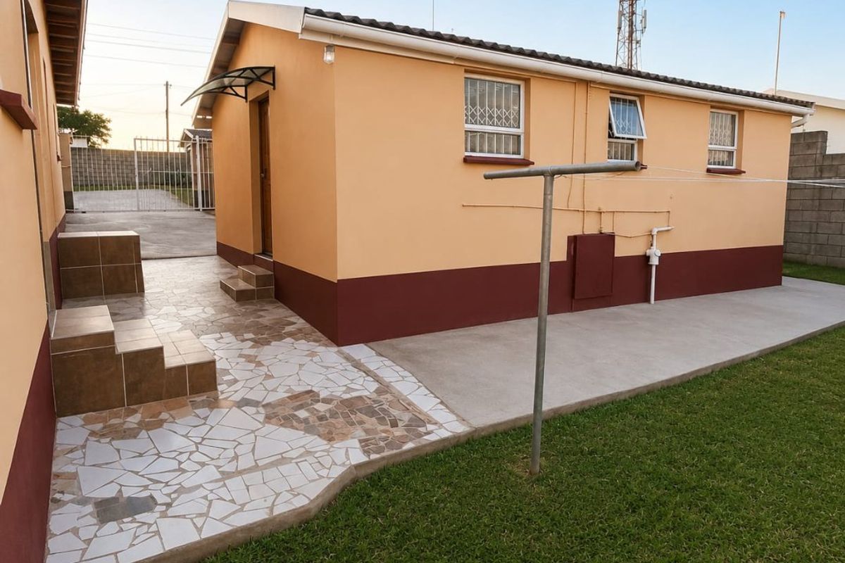 Rear exterior view of the property featuring a tiled patio area, concrete walkway, and a well-maintained lawn with secure boundary walling.
