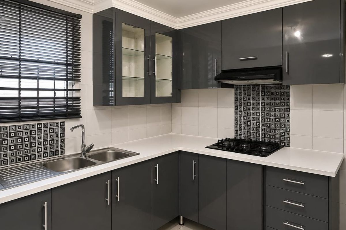 Modern kitchen featuring high-gloss grey cabinetry, white stone countertops, a gas hob with extractor, and a stainless steel double sink.