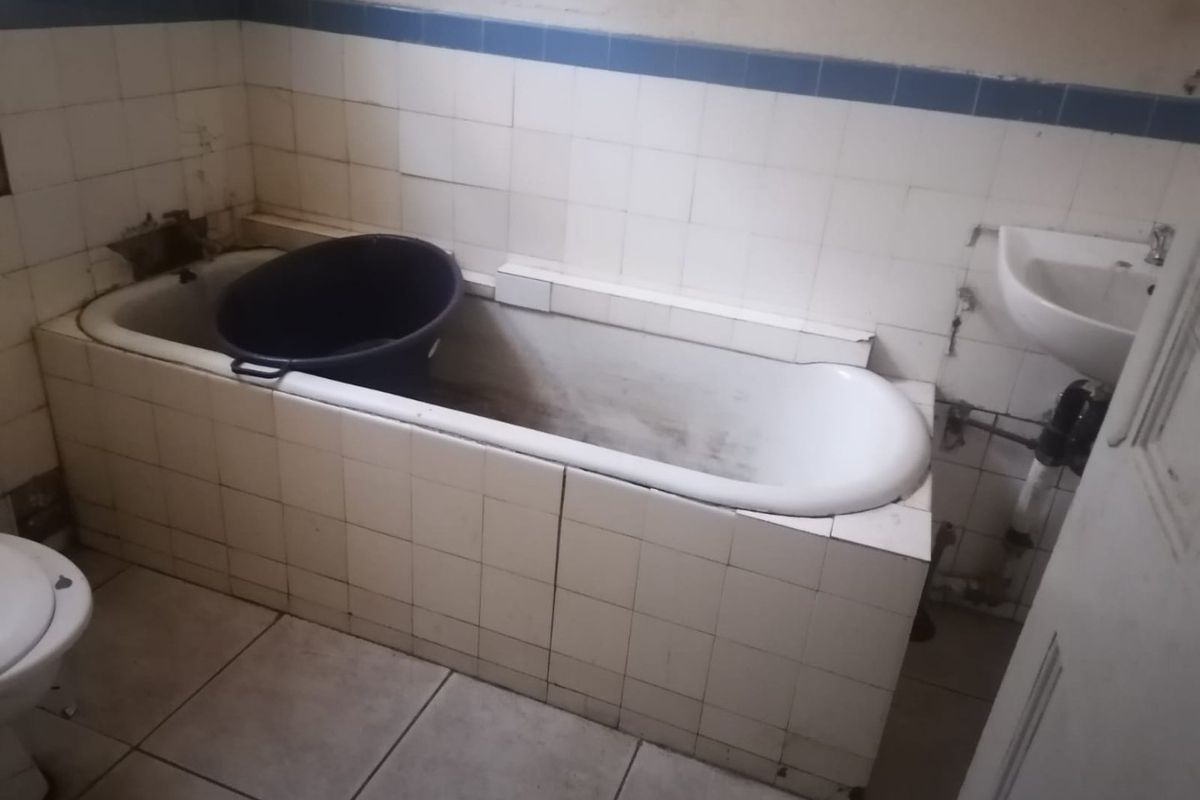 A dated bathroom featuring a tiled bathtub surround and wall-mounted basin, requiring significant renovation and cosmetic updates to restore functionality and appeal.