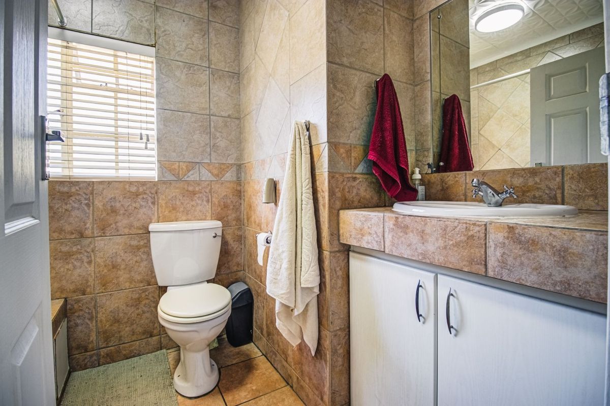 A functional bathroom featuring tiled walls and flooring, a vanity cabinet with a basin, and a window with fitted blinds.